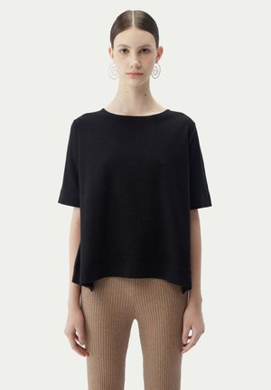 Haut noir à manches courtes avec un col rond, fabriqué à partir d'un tissu doux. Présente une coupe décontractée et des fentes sur les côtés pour faciliter les mouvements.