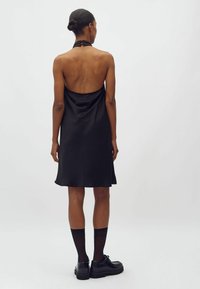 Mustapantaolka dress, jossa on avonainen selkäosa, valmistettu sileästä kankaasta. Siinä on kaareva helma ja se on yhdistetty mustiin sukkiin ja kenkiin.