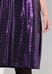 Robe en sequins violets avec une surface scintillante, présentant une coupe droite et un design fluide. Le gros plan montre une texture étincelante et des motifs.