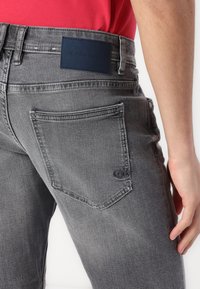 Jean en denim gris avec une coupe standard, présentant des poches arrière, une étiquette en cuir et une texture légèrement décolorée.