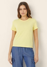 T-shirt giallo a maniche corte con scollatura rotonda. Tessuto morbido e leggero con una texture liscia. Abbinalo a pantaloni cargo blu.