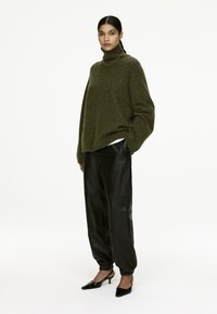 Olive green oversized turtleneck sweater made of soft material, paired with black leather baggy trousers and black heeled shoes.