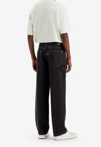 Svarta vida jeans med hög midja, med bakfickor och subtila sömdetaljer. I kombination med en ljusfärgad kortärmad skjorta.