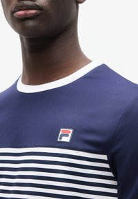 Κοντομάνικο πουκάμισο σε ναυτικό μπλε με λευκό ριγέ σχέδιο, διαθέτει λευκό γιακά και μικρό κεντητό λογότυπο Fila στο στήθος.