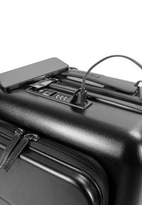 Zwarte harde koffer met een ingebouwde USB-poort, textuuroppervlak, dubbele ritsen en een gestroomlijnd ontwerp. Telefoon ligt bovenop de koffer.