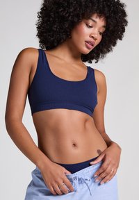 Navy ribbed bralette dengan leher bulat, tali yang lebar, dan pita tanpa jahitan. Dipadukan dengan celana piyama bergaris biru muda.