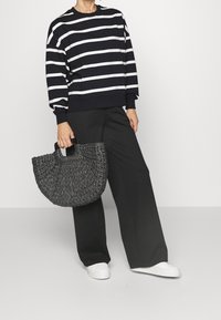 Sudadera de rayas en azul marino y blanco, corte holgado; pantalones negros de pierna ancha; bolso tejido gris texturizado con asas; zapatillas deportivas blancas.