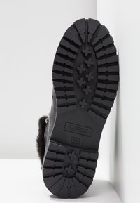 Suela exterior de goma negra con patrón de taco profundo, que presenta un logo rectangular y número de talla, diseñada para tracción y durabilidad.