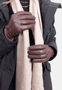 Brown leather gloves with a snug fit, featuring distinct stitching and subtle accents, held around a beige wool scarf.