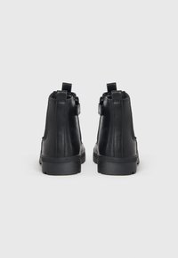 Black leather ankle boots with a smooth finish, featuring side zippers, pull tabs, and a textured rubber sole.
