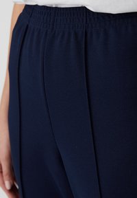 Marineblauwe sportbroek met een gestructureerde stof, voorzien van een elastische tailleband en subtiele plooien aan de zijkant voor extra ontwerpdetails.