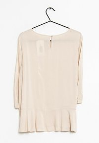 Blusa beige chiaro con orlo svasato, maniche lunghe e chiusura con bottone a occhio di bue sul retro. Realizzata in un tessuto morbido e leggero.