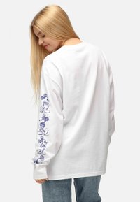 T-shirt bianca a maniche lunghe con schizzi di Topolino blu lungo la manica sinistra, realizzata in morbido cotone con design a girocollo.