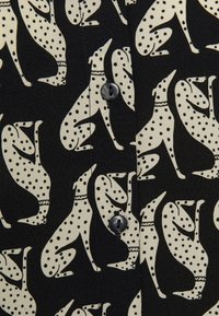 Tela negra con un patrón repetido de perros blancos con lunares; incluye un detalle de botón. La textura parece suave y lisa.