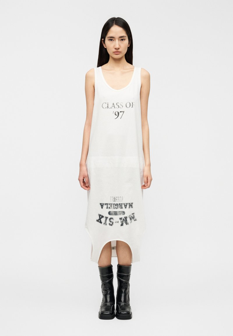 Robe blanche sans manches avec le texte "CLASS OF '97" en noir, présentant un ourlet légèrement arrondi et une coupe décontractée. Associée à des bottes noires.