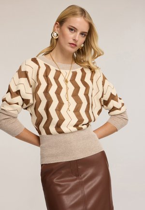 Strickpullover mit Zickzackmuster in Creme und Braun, ausgestattet mit einem gerippten Saum und Dreiviertelärmeln, kombiniert mit einem Rock aus braunem Leder.