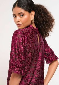 Bordové vyšívané šaty s kvetinovými vzormi; priehľadná látka; volánové rukávy; detail na chrbte v tvare otvoru; hladká textúra.