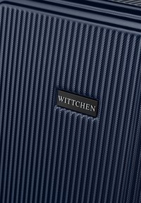 Valigia rigida blu con texture a righe verticali, dotata di una placca metallica nera con la scritta "WITTCHEN" sul davanti.