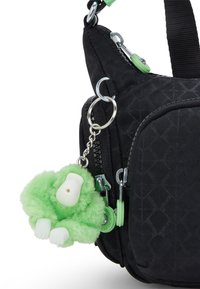 Borsa in tessuto nero con motivo a diamante, dotata di un portachiavi a forma di scimmia verde pelosa e tiretti verde. Accenti in metallo argentato visibili.