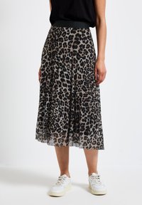 Gonna plissettata con motivo leopardato, dotata di una fascia elastica nera in vita e realizzata in tessuto trasparente, indossata con sneaker bianche. La gonna scende sotto il ginocchio.