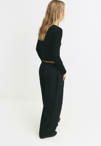 Musta pitkähihainen crop-top, joka on yhdistetty väljiin mustiin housuihin. Asusteessa on yksinkertainen muotoilu, pehmeä tekstuuri ja joustava vyötärö.