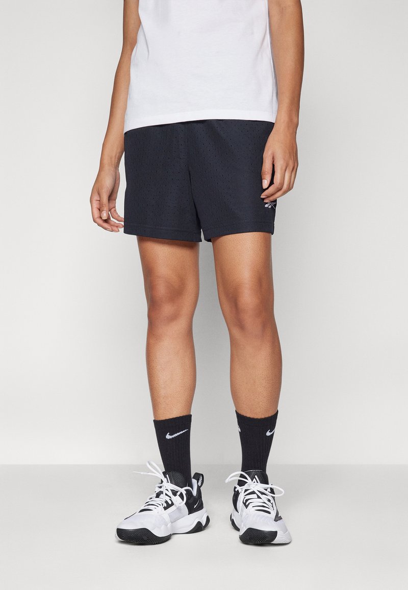 Juodi perforuoti sportiniai šortai su plokščiu juosmeniu, derinami su juodais ilgaamžiais kojiniais su balta Nike logotipu ir juodais bei baltais batais.