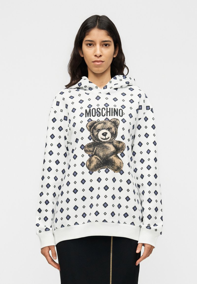 Λευκό φούτερ με κουκούλα, με γραφικό αρκουδάκι και κείμενο "MOSCHINO", με διακοσμητικό μοτίβο διαμαντιών σε μπλε χρώμα. Απαλό ύφασμα και άνετη εφαρμογή.