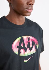 Svart bomull t-shirt med en färgglad gradient "Air" logotyp i rosa och gröna accenter. Klassisk rundhalsad design.