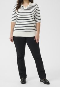 Krótki rękaw, kremowy sweter w granatowe paski, z dekoltem w kształcie litery V. W połączeniu z czarnymi spodniami prostymi i czarnymi loafersami.