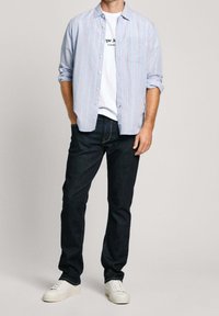 Vaaleansininen raidallinen nappipaita valkoisen t-paidan päällä, yhdistetty tummiin farkkuihin ja valkoisiin lenkkareihin. Sisältää rintataskun ja käärityt hihat.