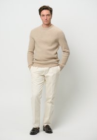 Beige ribbstickad tröja, krämfärgade byxor, svarta loafers. Tröjan har rund halsringning och en åtsittande design. Byxorna har rak passform och är lätta.