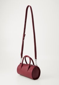 Burgundy leather handbag with a rounded shape. Features dual top handles, an adjustable shoulder strap, and a zip closure. Textured finish.