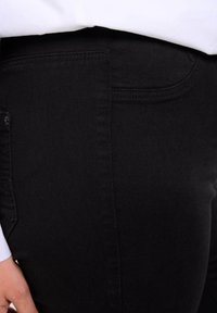 Jean en denim noir avec une texture lisse, coupe slim, poches latérales et coutures renforcées le long des coutures.
