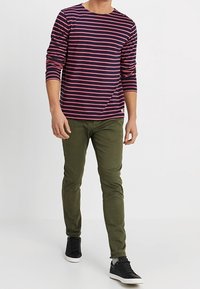 Long-sleeve navy shirt with pink horizontal stripes, paired with olive green slim-fit pants and black sneakers, featuring white soles.