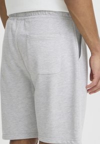 Shorts en coton gris avec une ceinture élastique, dotés d'une unique poche arrière et d'un tissu doux et texturé. L'ourlet est propre et soigné.
