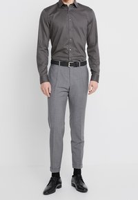 Szara koszula na guziki z długimi rękawami, w połączeniu z jasnoszarymi, dopasowanymi eleganckimi spodniami i czarnymi butami, wszystko uzupełnione czarnym paskiem.