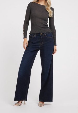 Un jean large bleu foncé en denim, associé à un haut à manches longues gris foncé côtelé avec des accents de boutons aux manches.