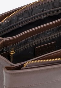 Wnętrze brązowej torby skórzanej z wieloma przegródkami, w tym z sekcją na zamek błyskawiczny, zamkiem w kolorze złota oraz czarną podszewką z logo.