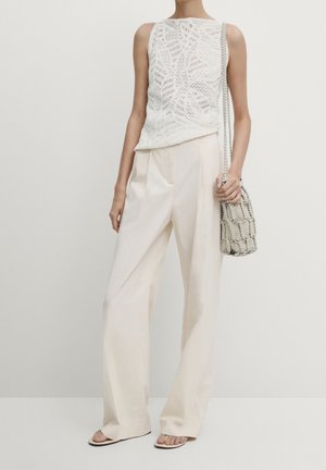 Biały dzianinowy top na ramiączkach z misternym wzorem, w połączeniu z luźnymi kremowymi spodniami i teksturowaną szaro-brązową torbą.