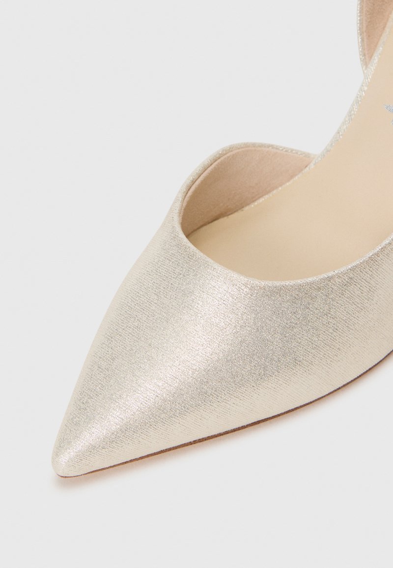 Puntige pump in metallic gouden stof met een gladde textuur en uitgesneden zijkanten. Heeft een beige binnenzijde en een dunne zool.