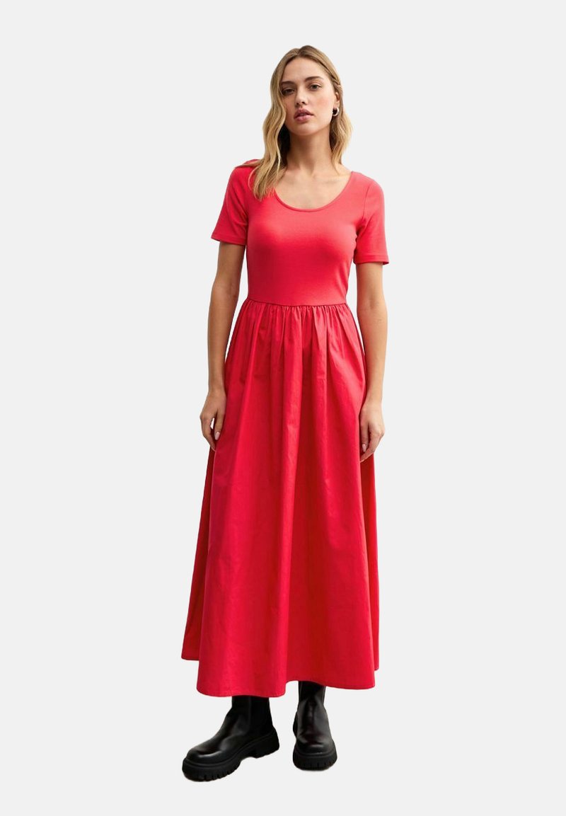 Vestido maxi rojo con mangas cortas, cuello redondo y cintura fruncida. Hecho de un material ligero, combinado con botas negras de suela gruesa.