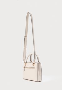 Kompaktne beež käekott tekstuurse materjaliga, millel on peal käepide, reguleeritav õlakõrvarõngas ja esiküljel tõmblukuga tasku kuldsete detailidega.