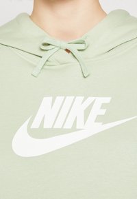 Person som bär en ljusgrön hoodie med en vit Nike-logotyp och dragsnören knutna i en rosett vid halsen.