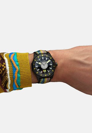Black octagonal watch with yellow accents, transparent dial, and colorful fabric strap, worn on a wrist with a patterned sweater cuff.