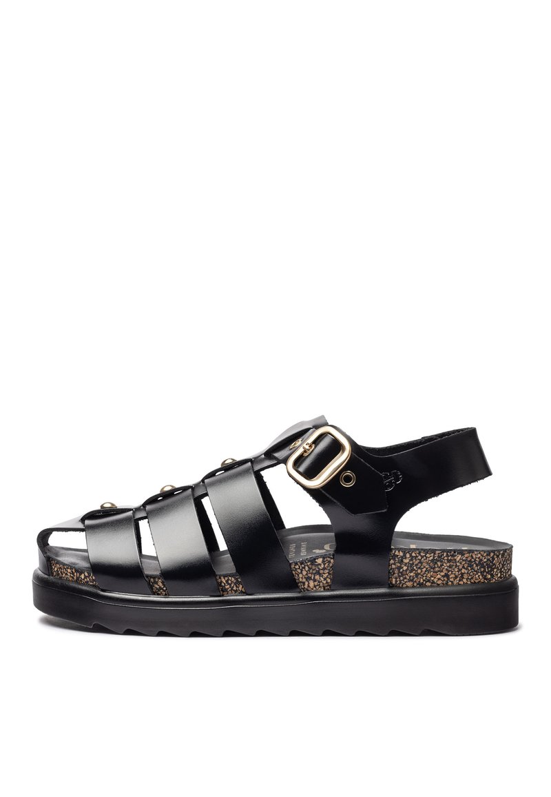 Sandal de tiras negras con un acabado brillante, que presenta un acento de hebilla, plantilla de corcho y suela texturizada negra. Diseño de punta abierta.
