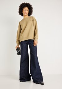 Krémová mikina s kulatým výstřihem, volný střih a vyšitým textem. Tmavé denimové kalhoty širokého střihu, černá kabelka s stříbrnými studny.