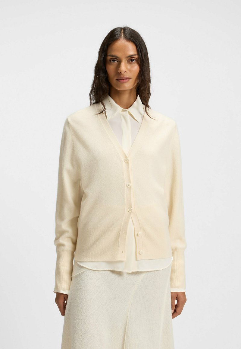 Cream-colored cardigan made of soft fabric, featuring a V-neck, long sleeves, and a button-down front for closure.