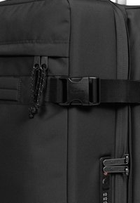 Černý kufr na kolečkách vyrobený z texturované tkaniny, se dvěma zipovými táhly, bočním sponou a kombinovaným zámkem na přední straně.