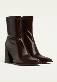 Bottines en cuir verni marron, avec un bout pointu, un talon carré et une fermeture éclair sur le côté. Texture lisse avec une finition brillante.