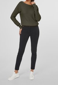 Pull en maille vert olive avec un motif texturé, associé à un pantalon noir ajusté et des baskets blanches. Design simple et moderne.